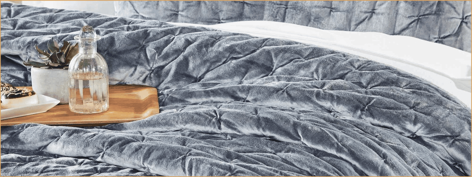 Wide banner image of a velvet quilt on a bed, styled with decor on a wooden tray.