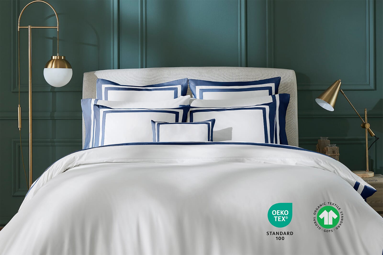 White and navy luxury bedding styled on a bed with certification icons in an elegant green bedroom.