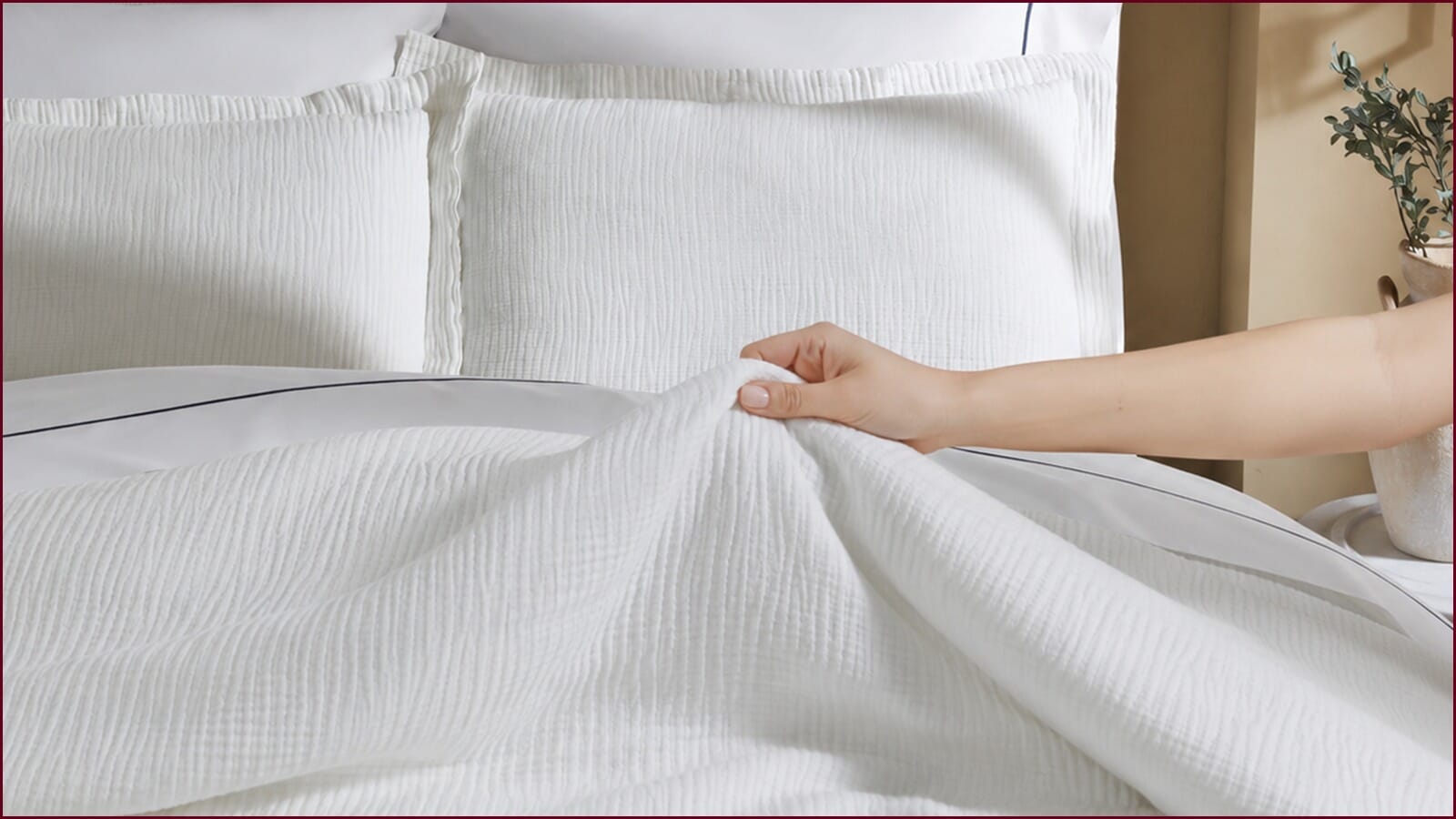White textured bedding with a hand lifting the soft fabric to show its lightweight, breathable feel.